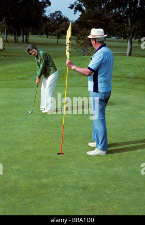1980ER JAHRE ÄLTERES PAAR SPIELT GOLF FRAU SETZEN AUF GRÜN Stockfoto