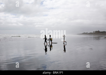 Schwimmer und Body Boarder zu Fuß bis zum Meer am Muriwai Beach, Neuseeland. Stockfoto