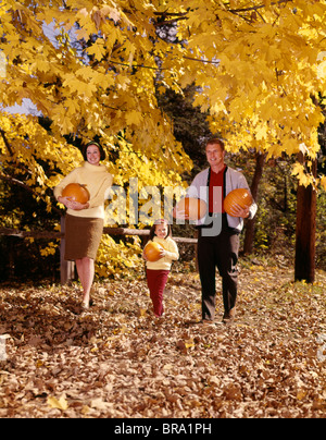 1960ER JAHREN WALD LÄCHELND FAMILIE TRIO VATER-MUTTER-TOCHTER GEHEN IM HERBST TRAGEN KÜRBISSE Stockfoto