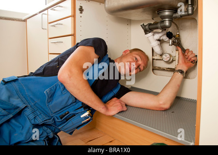 Heizungs- und Sanitär-Techniker reparieren die undichten Rohren unter der Küchenspüle Stockfoto