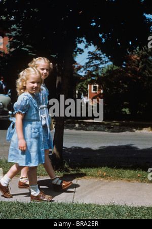 1950ER JAHREN ZWEI KLEINE MÄDCHEN, DIE ZU FUß TRAGEN BLAUE KLEIDER AM ERSTEN TAG DER SCHULE 1951 Stockfoto