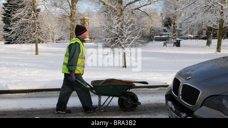 Des Rates Arbeiter schiebt eine Schubkarre voller Korn vorbei an einem geparkten BMW bereit, das Salz auf einer verschneiten Straße im Winter Schaufel Stockfoto