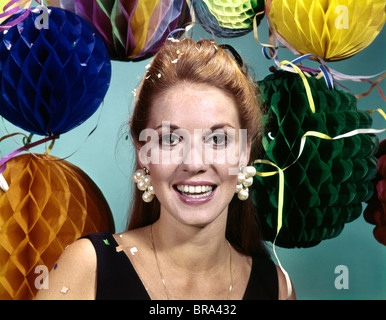 1960ER JAHREN LÄCHELNDE FRAU GROßE OHRRINGE HINTERGRUND PARTY DEKORATIONEN KONFETTI LUFTSCHLANGEN FEIER RETRO- Stockfoto
