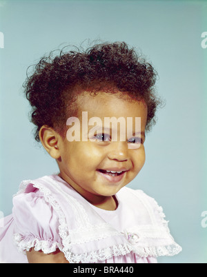 1960ER JAHRE PORTRAIT LÄCHELND AFRO-AMERIKANISCHE KLEINKIND MÄDCHEN LÄCHELT GLÜCKLICH TRAGEN ROSA SPITZEN KLEID Stockfoto
