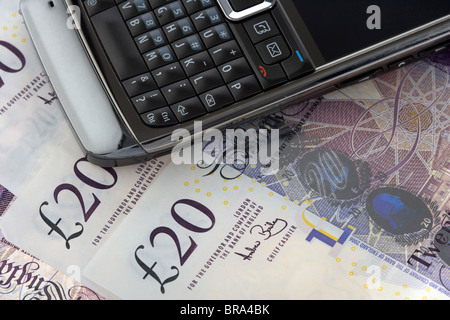 Mobile Handy Smartphone auf einen Haufen von zwanzig Pfund Sterling Banknoten Stockfoto