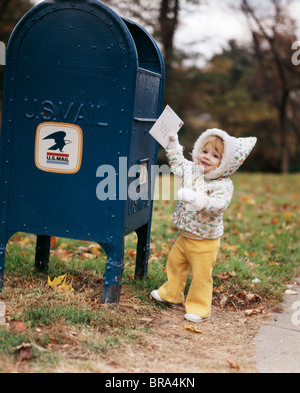 1970ER JAHREN LÄCHELND KLEINKIND MÄDCHEN TRAGEN KAPUZEN JACKE BIS ZU BRIEF IN MAIL DROPBOX Stockfoto