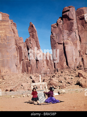 1960ER JAHREN NAVAJO MUTTER & TOCHTER AM WEBSTUHL WEBEN HINTERGRUND DER ROTEN FELSEN KLIPPEN VON INDIANER-RESERVAT Stockfoto