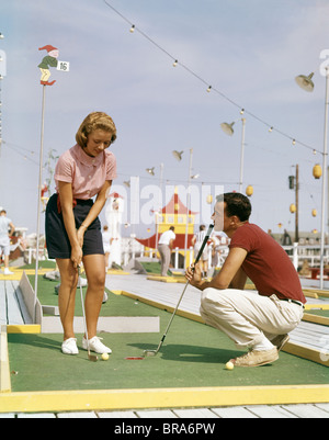 1950S 1960S JUNGES PAAR MANN FRAU SPIELEN MINIGOLF SOMMER UNTERHALTUNG FREIZEIT DATUM KERL KNIET GAL PUTTS KURS SPIELEN Stockfoto