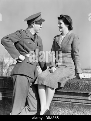 1940ER JAHREN GLÜCKLICHE PAAR MANN TRAGEN ARMEE UNIFORM FRAU SITZEN AUF STEINMAUER Stockfoto