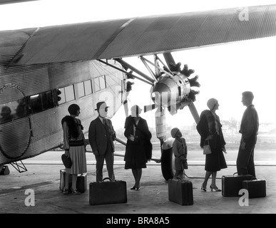 1920S 1930S GRUPPE VON PASSAGIEREN STEHEN UNTER FLÜGEL DER FORD TRI-MOTOR FLUGZEUG MIT GEPÄCK Stockfoto