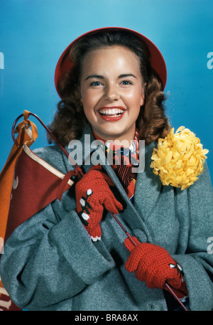 1940S 1950S LÄCHELNDE JUNGE FRAU MIT COLLEGE WIMPEL HOMECOMING CORSAGE MAMA MIT GRAUEN MANTEL & ROTEN HANDSCHUHEN Stockfoto