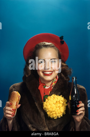 1940S 1950S LÄCHELND TEEN HIGH SCHOOL COLLEGE GIRL HOLDING HOT DOG & SODA TRAGEN GELBE HOMECOMING FOOTBALL SPIEL CHRYSANTHEME Stockfoto