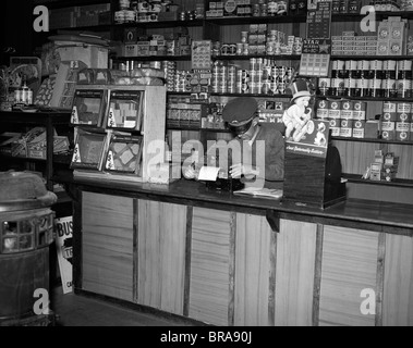 1930ER JAHRE MANN HINTER DER THEKE IM ALLGEMEINEN SPEICHERN MIT SCHREIBMASCHINE Stockfoto