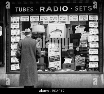 1940ER JAHRE MANN BETRACHTEN SCHAUFENSTER DES RADIOS ZUM VERKAUF IN NEW YORK CITY Stockfoto