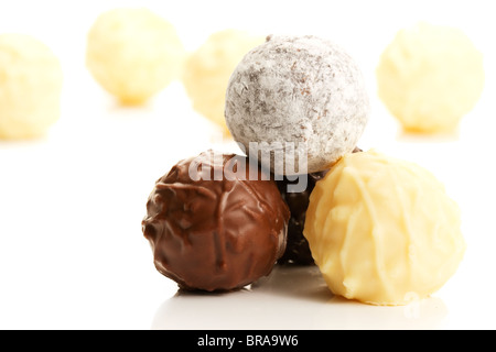 Stapel von verschiedenen Trüffel Pralinen vor gelben Trüffel auf weißem Hintergrund Stockfoto