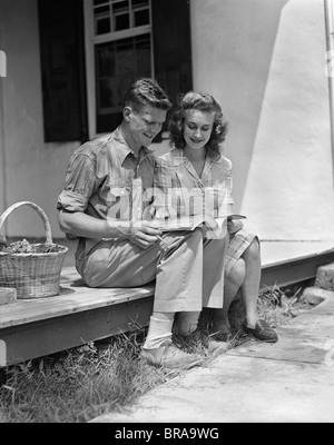 1940ER JAHRE MANN FRAU SITZT AUF DER VERANDA DES BAUERNHAUSES LESUNG KATALOG Stockfoto