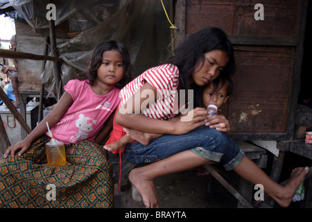 Ein 14 Jahres altes Mädchen sitzt mit ihren Geschwistern auf der Veranda ihres Hauses in einem Slum in Phnom Penh, Kambodscha. Stockfoto