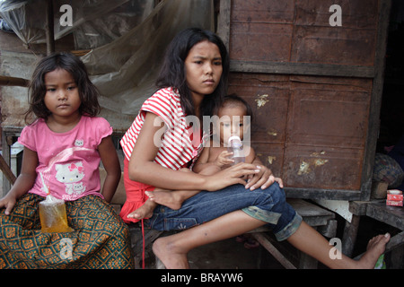 Ein 14 Jahres altes Mädchen sitzt mit ihren Geschwistern auf der Veranda ihres Hauses in einem Slum in Phnom Penh, Kambodscha. Stockfoto