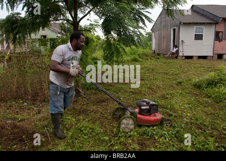 Ein Mann schneidet Unkraut aus den vom Hof seines teilweise umgebauten Hauses in New Orleans, Louisiana Ninth Ward. Stockfoto