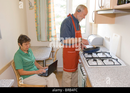 Älteres Paar in Küche, Mann Kochen beim Musikhören, Frau mit netbook Stockfoto