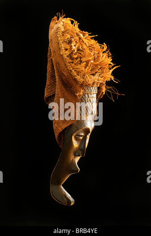 Geschnitzte afrikanische Stammes-Holzmaske, dunklem Holz mit Stroh und Tuch Kopfschmuck. Afrika, Stamm, Foto von Seite im studio Stockfoto