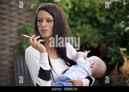 Mutter in ihr 20 ist eine Zigarette halten und ihr Baby in ihren Armen Rauchen. Stockfoto