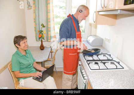 Älteres Paar in Küche, Mann Kochen beim Musikhören, Frau mit netbook Stockfoto