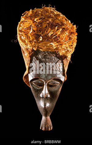 Geschnitzte afrikanische Stammes-Holzmaske, dunklem Holz mit Stroh und Tuch Kopfschmuck. Afrika, Stamm, Foto von vorne im studio Stockfoto