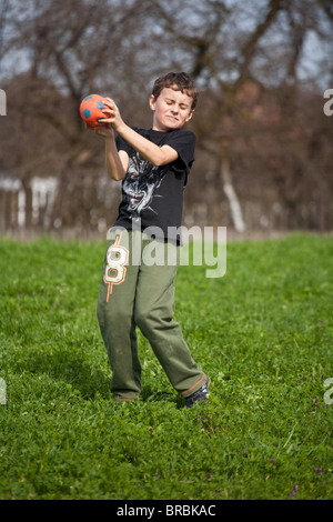 Lustige junge Grimassen beim Fang des Ball im freien Stockfoto