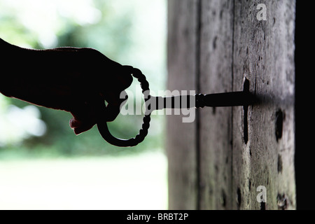 Silhouette von Frauenhand drehen einen riesigen Schlüssel in einer alten Kirche Holztür. Stockfoto