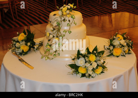 Eine traditionelle dreistöckigen weiße Hochzeitstorte auf Tisch an der Rezeption mit gelben und weißen Rosensträuße. Dorset, UK 2009 Stockfoto
