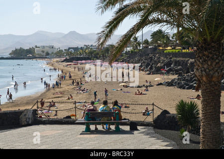 dh Strand PUERTO DEL CARMEN LANZAROTE Touristen sitzen auf Promenade Bank mit Blick auf Strand Stockfoto