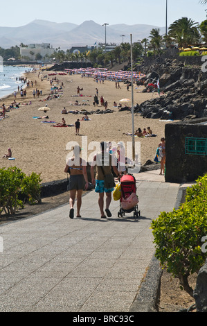 Dh Strand PUERTO DEL CARMEN LANZAROTE Touristische paar Kinderwagen hinunter zum Strand junge Urlaub Familienurlaub Stockfoto