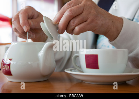 Person in einem Café Mania Café rühren Kaffee in einer Teekanne mit Tasse und Untertasse. Großbritannien, Großbritannien. Stockfoto