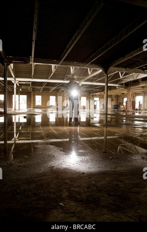Abriss-Worker Holding Taschenlampe im alten industriellen Gebäude mit Wasserpfütze im Stock, Philadelphia, USA Stockfoto