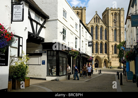 Menschen Touristen Besucher außerhalb Geschäfte und Kathedrale von Kirkgate in Sommer Ripon North Yorkshire England Großbritannien GB Groß Großbritannien Stockfoto