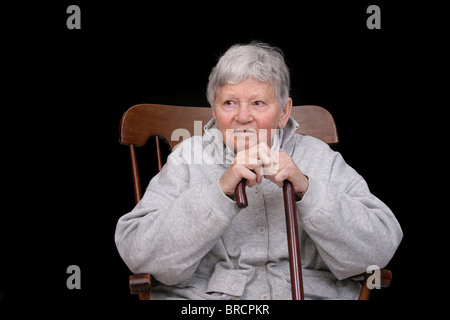 eine ältere Erwachsene Frau saß in einem Schaukelstuhl halten ihres Stocks Stockfoto