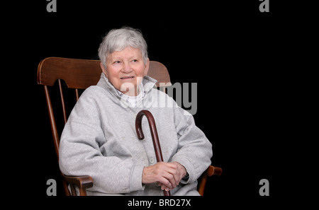 eine ältere Erwachsene Frau saß in einem Schaukelstuhl halten ihres Stocks Stockfoto