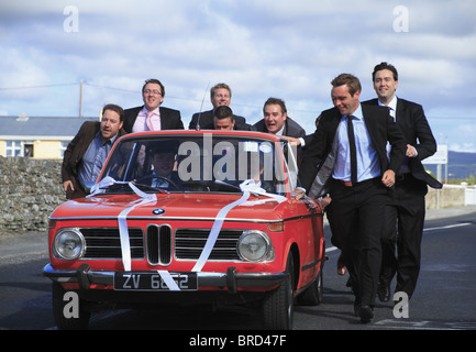 Hochzeitsgäste schieben das Hochzeitsauto aufgeschlüsselt nach Hause. Stockfoto