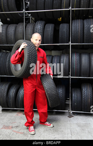 Ein motivierter Arbeiter in einem Reifen-Workshop mit zwei Reifen. Stockfoto