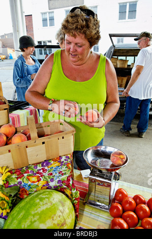 Frau mit einem Gewicht von frischen Pfirsichen inmitten anderer Produkte am Wochenmarkt in New Albany, Indiana Stockfoto