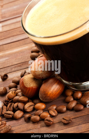 Kaffeebohnen und Haselnüsse in der Nähe von Espresso in einer kurzen Glasschale auf hölzernen Hintergrund Stockfoto