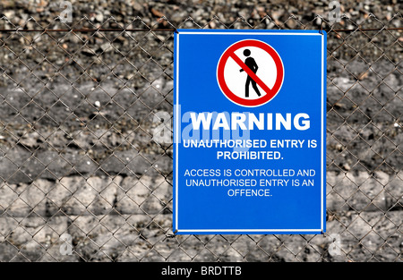 Ein Warnschild auf einem Drahtzaun mit blauem Hintergrund und eine schwarze Figur einer Person mit einem roten Kreis aufgeschlitzt Stockfoto