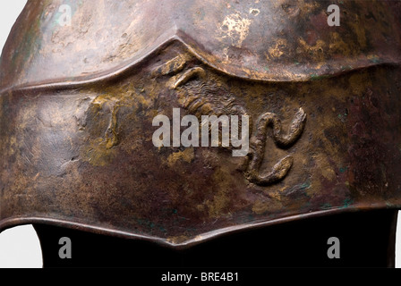 Ein Chalcidian-Helm mit griffin-wappen, 4. Jahrhundert v. Chr. Hoher, verlängerter bronzener Schädel, ähnlich dem auf phrygischen Helmen, überragt von einem Scheitel mit wellenförmigen Stacheln und tröpfchenarmer Dekoration. Breites, abgelegenes Brühenfeld mit einem Fragment eines zentralen Gorgoneions, das von zischenden Schlangen umgeben ist. Kurzhalsschutz. Geprägte Voluten über den Ohrausschnitten und ein reich verzierter Flügel, der auf der linken Seite vernietet ist (der andere fehlt). Zwei ungewöhnliche, herzförmige Wangenstücke mit Kinnschlingen, die nach innen genietet sind. Eine Schriftrolle und das Segment eines Bogens über jedem der Formerl, Stockfoto