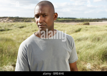 Nachdenklicher junger Mann steht am Strand zwischen Dünen Stockfoto