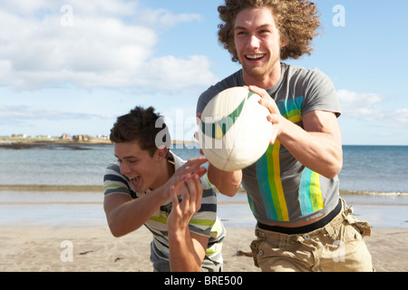 Zwei Jungs im Teenageralter Rugby zu spielen, am Strand zusammen Stockfoto