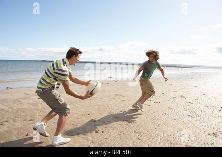 Zwei Jungs im Teenageralter Rugby zu spielen, am Strand zusammen Stockfoto