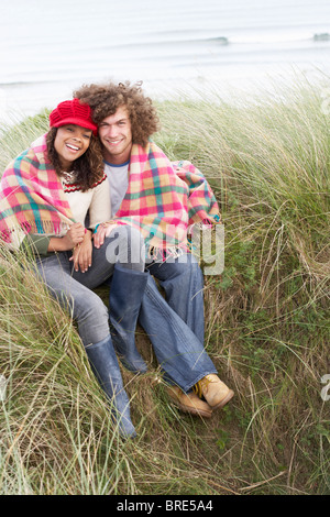 Junges Paar sitzt In Sanddünen In Decke gehüllt Stockfoto