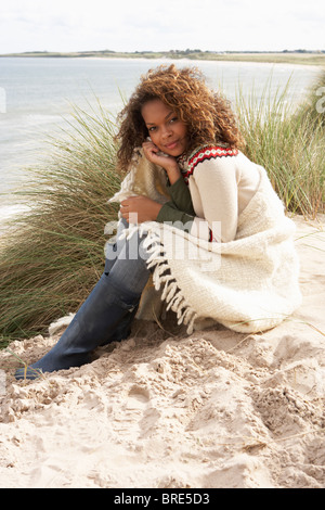 Junge Frau sitzt In Sanddünen In Decke gehüllt Stockfoto