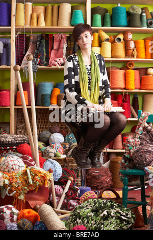 Junge Frau sitzt auf Schemel mit Stricknadeln vor Garn Display Stockfoto